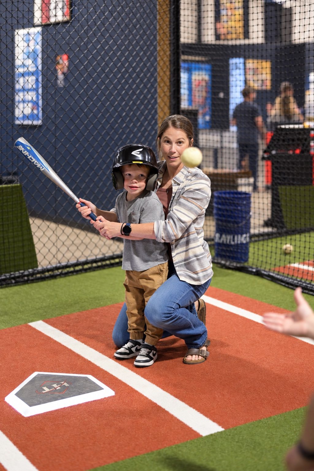 An adult helping a young child grip the bat in a Hitters batting cage